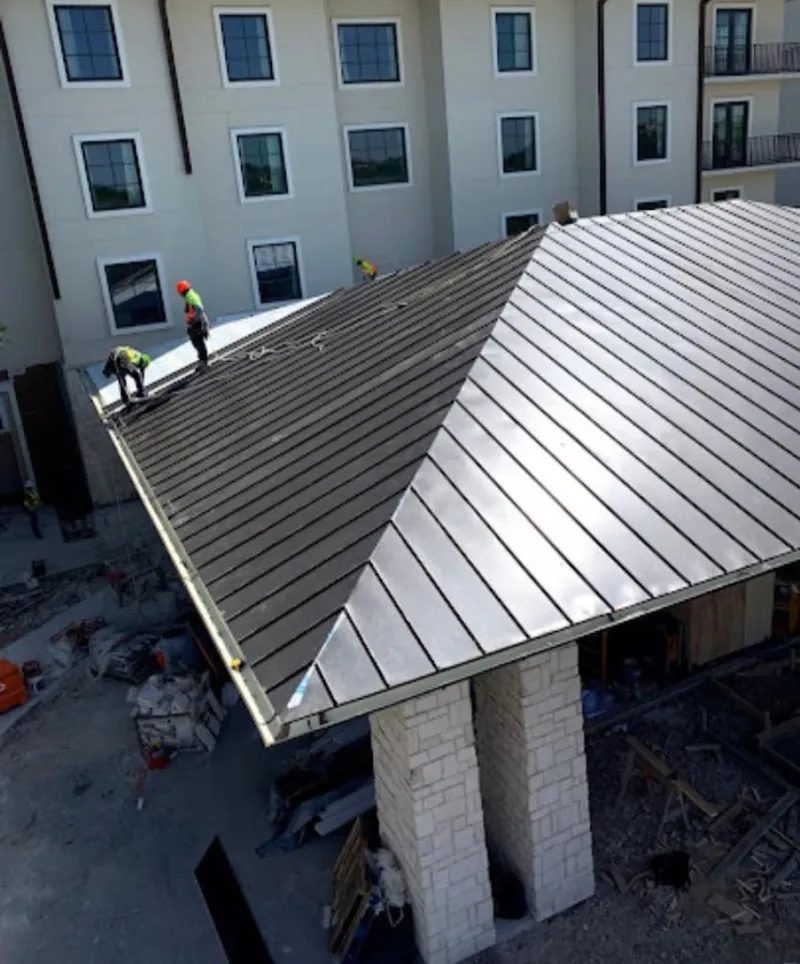 Crew installing standing seam metal roof panels on a commercial project in Iola